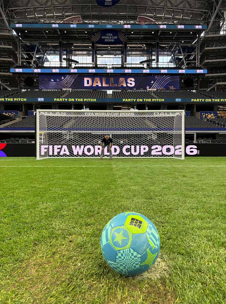 A soccer ball on the front of a goal, with a goalkeeper and stadium banners showcasing "DALLAS" and "FIFA WORLD CUP 2026"