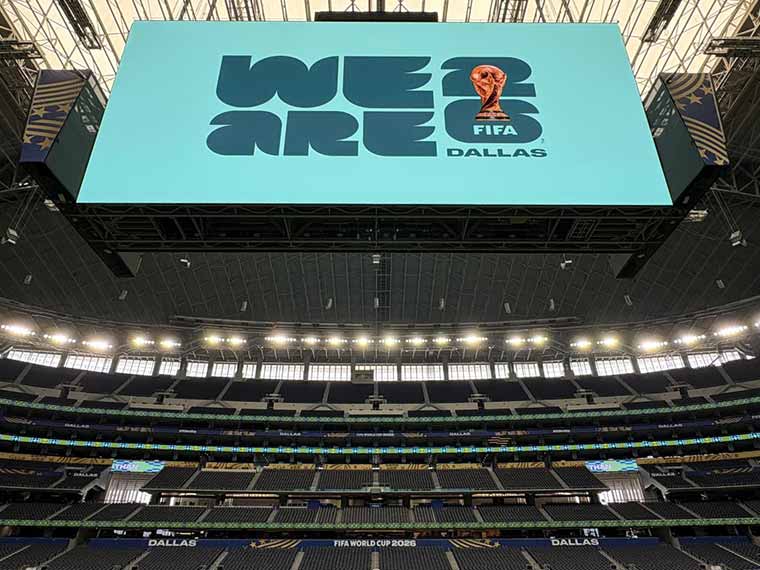 A large digital display in a stadium reads "WE ARE 6" with the FIFA trophy illustration